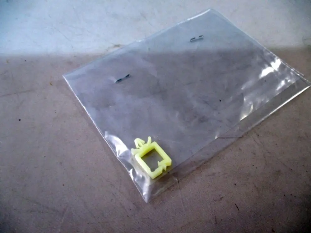 Transparente Plastiktüte mit einer gelben Halterung und zwei kleinen Metallklammern. Produkt von Wolf, möglicherweise Teil eines Kabelmanagementsystems.
